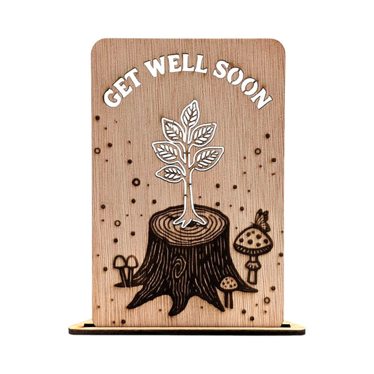Houten wenskaart met lasergegraveerd ontwerp van een jonge scheut die uit een boomstronk groeit, de tekst 'GET WELL SOON', paddenstoelen en een vlinder op natuurlijke houtnerf.