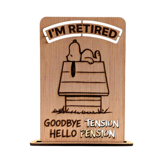 Houten pensioenkaart met een gravure van een hond die op een hondenhok slaapt en de uitgesneden tekst 'I'M RETIRED' en 'GOODBYE TENSION HELLO PENSION'.