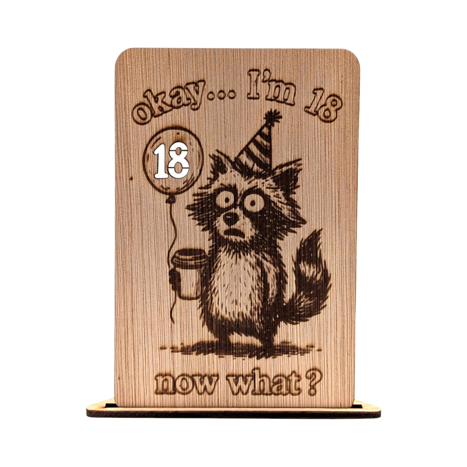 Houten verjaardagskaart 18 jaar met een grappige gravure van een wasbeer met feestmuts en koffie, inclusief de tekst 'okay... I'm 18 now what?'.