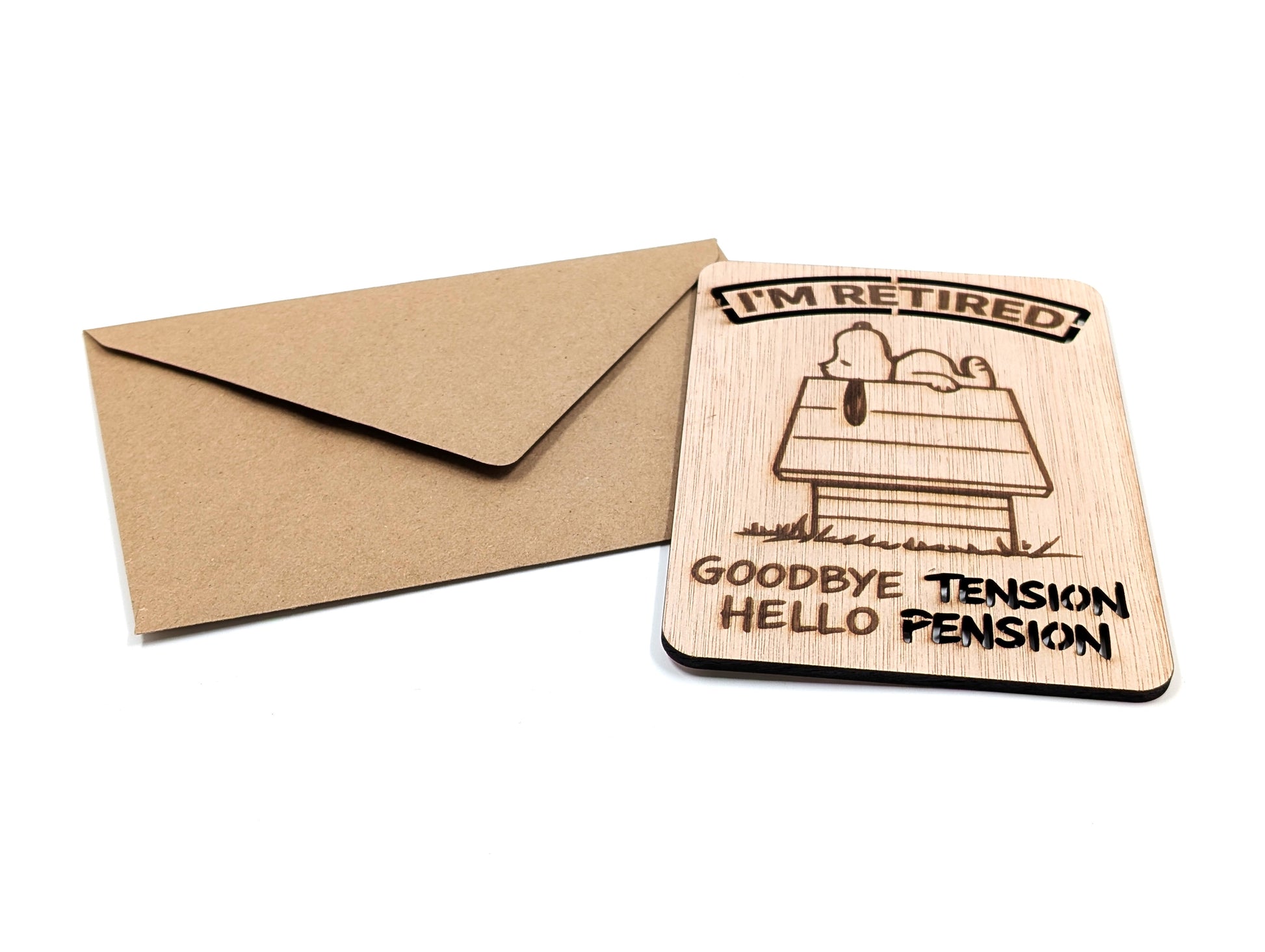Humoristische houten wenskaart voor pensioen liggend naast een bruine kraft envelop op een witte achtergrond.
